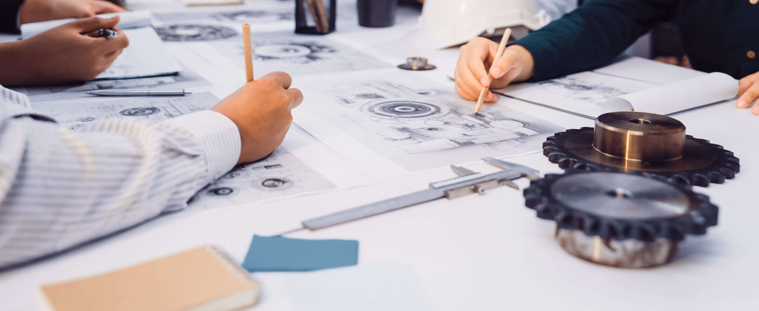 Pr&uuml;fung und Freigabe technischer Zeichnungen f&uuml;r den Prototypenbau. Ingenieure analysieren Zeichnungen f&uuml;r Entwicklungsmuster direkt am Tisch mit Messschieber und Metall-Bauteilen.